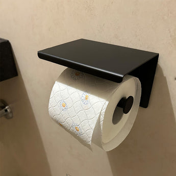 Un rouleau de papier toilette blanc au motif marguerite est suspendu à l'ensemble WC Tygo Black (sans perçage) de yessential.fr, monté sur un mur beige.