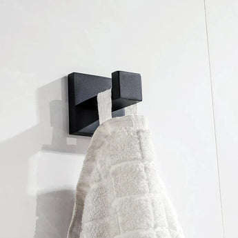 L'ensemble de WC Venzo Black de yessential.fr comprend un élégant crochet mural carré en métal qui maintient une serviette texturée blanche contre des carreaux blancs - un ajout moderne idéal à vos accessoires de salle de bain.