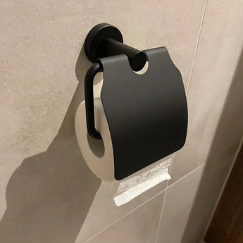 Un ensemble de toilettes Quirino Black de yessential.fr est monté sur un mur carrelé beige, avec son porte-papier toilette et son couvercle pour fixer un rouleau - pratique et élégant pour votre ensemble d'accessoires de salle de bain.