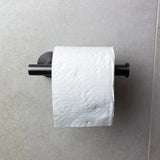 Un rouleau de papier toilette blanc avec un motif ondulé est suspendu au porte-rouleau de papier toilette Tino Gunmetal de yessential.fr, un ajout élégant aux accessoires de toilette modernes, monté sur un mur carrelé gris clair.