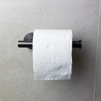 Un rouleau de papier toilette blanc avec un motif ondulé est suspendu au porte-rouleau de papier toilette Tino Gunmetal de yessential.fr, un ajout élégant aux accessoires de toilette modernes, monté sur un mur carrelé gris clair.