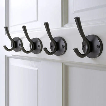 Quatre élégantes patères Eduardo Gunmetal de yessential.fr sont montées en rangée sur une porte à panneau blanc, chacune fixée avec deux vis. Les crochets sont uniformément espacés et parfaitement alignés.