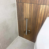 Un ensemble de toilettes Pacho en acier inoxydable de yessential.fr est monté verticalement sur un mur de salle de bain en bois sans rouleau de papier toilette. Le sol carrelé gris clair et les toilettes visibles laissent entrevoir de l'espace pour d'autres articles de la collection d'accessoires de salle de bain yessential.fr.