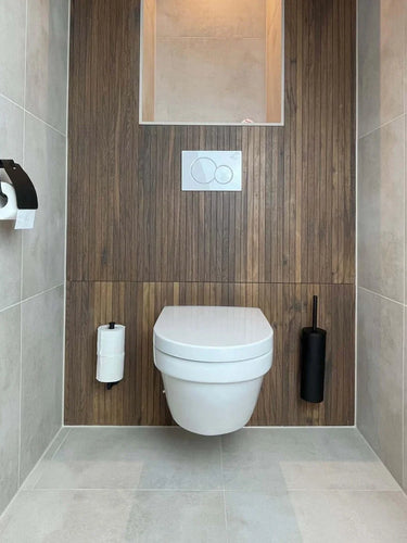 Salle de bain moderne et minimaliste avec toilettes suspendues, mur avec panneaux en bois, porte-papier toilette intégré à gauche et brosse WC Branco Black noire de yessential.fr à droite. Le sol et les murs carrelés gris clair complètent le look.