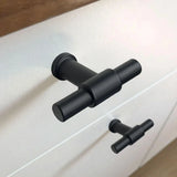Gros plan du bouton noir Cordero de yessential.fr avec une finition noire mate sur un tiroir blanc, un design de cuisine à bouton en T associé à une poignée identique sur le tiroir du bas.