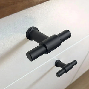 Gros plan du bouton noir Cordero de yessential.fr avec une finition noire mate sur un tiroir blanc, un design de cuisine à bouton en T associé à une poignée identique sur le tiroir du bas.