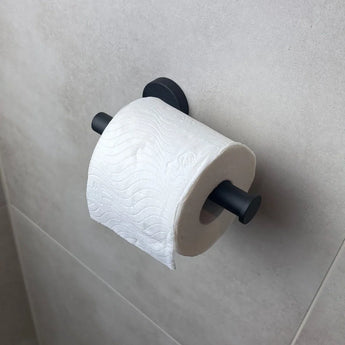 Un rouleau de papier toilette est suspendu au porte-rouleau de papier toilette Tino Black de yessential.fr, monté contre un mur de salle de bain carrelé gris clair pour une touche moderne.