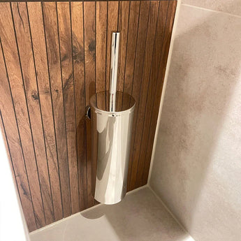 Le porte-brosse de toilette Branco Chrome de yessential.fr a une poignée argentée brillante, fixée au mur contre des panneaux de bois verticaux à côté des murs et du sol carrelés beige clair.