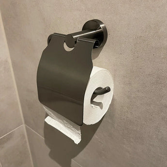 Un rouleau de papier toilette posé sur un support métallique avec couvercle ajoute une touche décalée à cette salle de bain moderne. Le mur de carrelage de couleur claire contraste avec l'ensemble WC Quirino Gunmetal de yessential.fr pour un look contemporain.