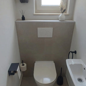 Une salle de bain moderne et minimaliste avec la série Elarbo Black de yessential.fr : toilettes suspendues, anneau porte-serviettes noir mat gain de place, porte-papier toilette, brosse WC noire, petite vasque et décor sur rebord avec vase et diffuseur à roseaux.